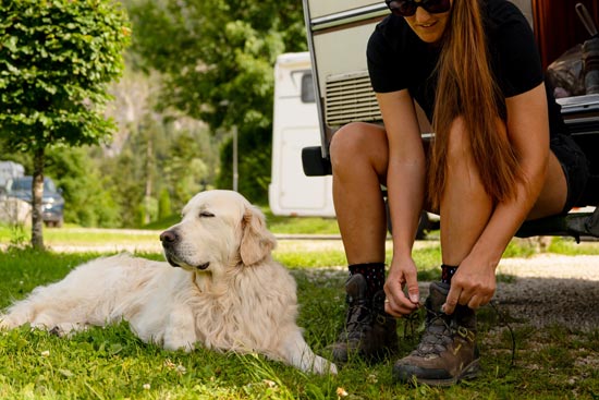 Detailfoto Camperin schnürt sich die Bergschuhe, daneben ihr Hund Detailfoto Camperin schnürt sich die Bergschuhe, daneben ihr Hund