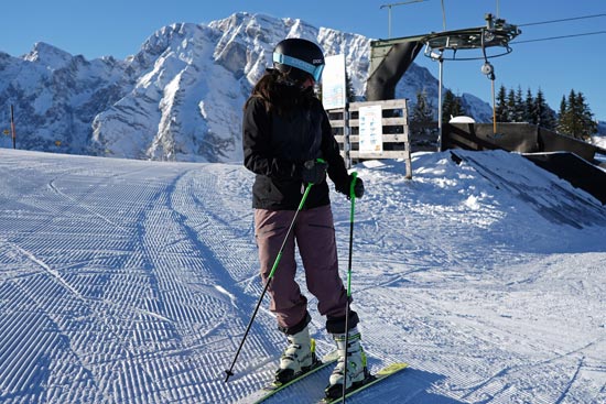Skifahrerin bei sonnigem Wetter auf der Piste, der Lift und die Berge im Hintergrund Skifahrerin bei sonnigem Wetter auf der Piste, der Lift und die Berge im Hintergrund