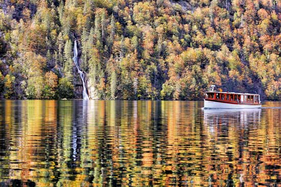 Herbstliche Stimmung am Königssee, Boot im Vordergrund, Wasserfall im Hintergrund