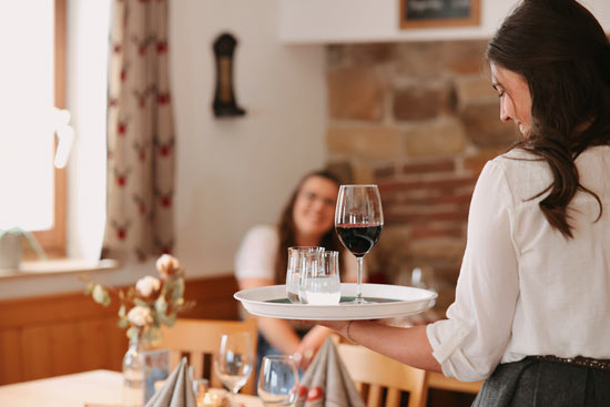 Kellnerin serviert Rotwein, im Hintergrund der Restaurantbereich Kellnerin serviert Rotwein, im Hintergrund der Restaurantbereich