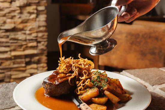 A close-up of an onion roast being topped with sauce.